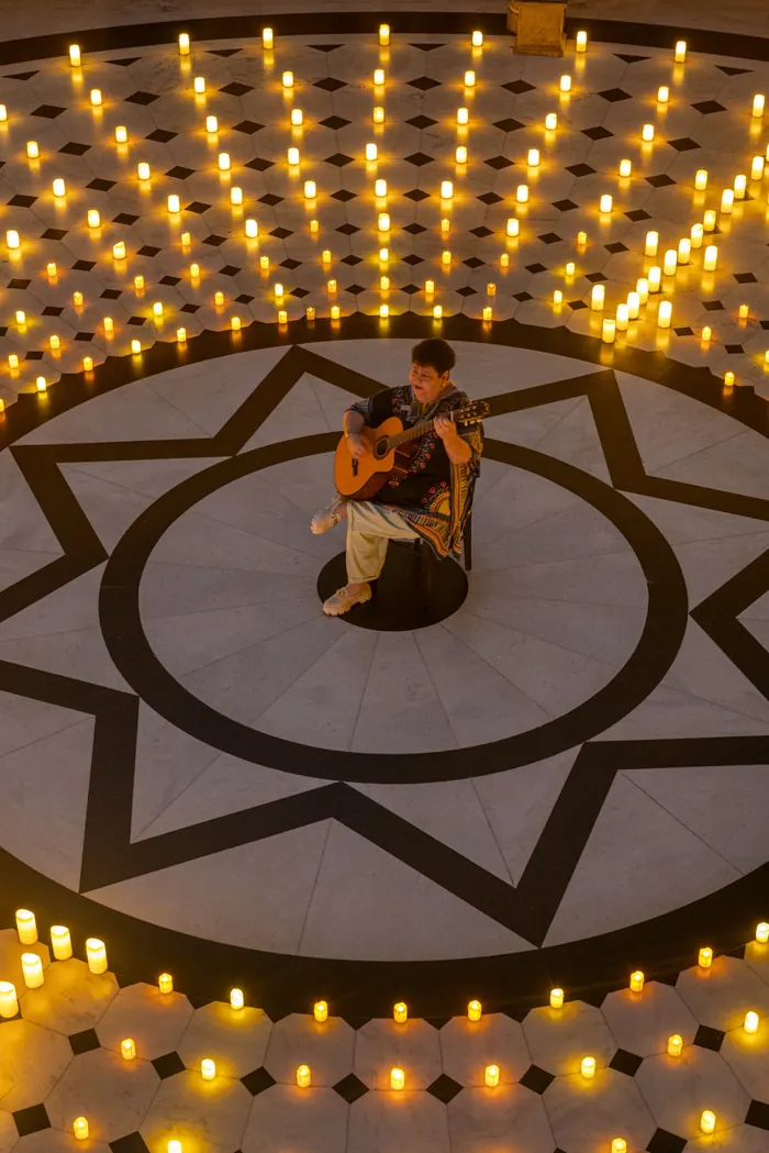 Pessoa tocando violão em um salão com velas dispostas no piso